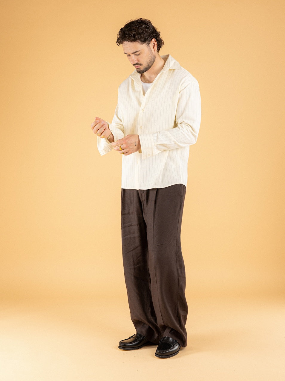 Man wearing oversized cream pinstripe shirt with black pleated trousers - Émilio SS26