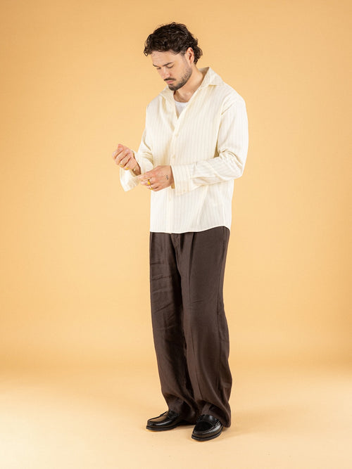 Man wearing oversized cream pinstripe shirt with black pleated trousers - Émilio SS26